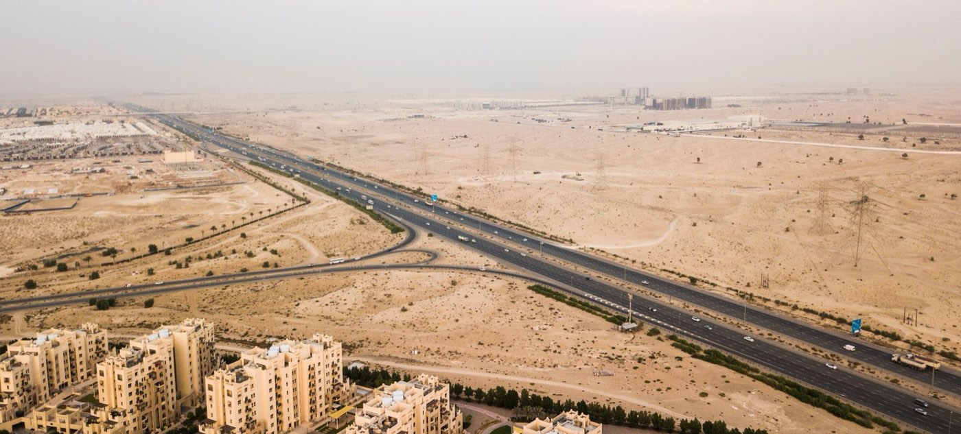Desert plots along a highway with low-rise buildings, Dubai